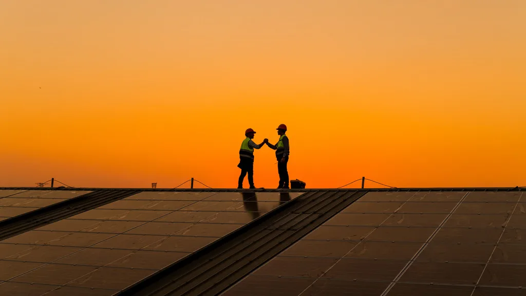 Trabalhadores sobre painéis solares ao pôr do sol, representando o uso de fontes de energia renováveis no setor elétrico brasileiro.