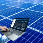 Pessoa utilizando notebook com sistema de monitoramento de energia solar em tempo real, em frente a painéis solares azuis.