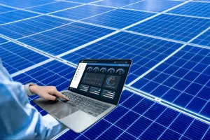 Pessoa utilizando notebook com sistema de monitoramento de energia solar em tempo real, em frente a painéis solares azuis.